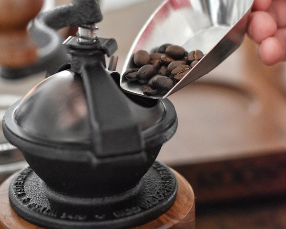 Scooping fresh roasted coffee beans into the Camano Coffee Mill manual coffee grinder