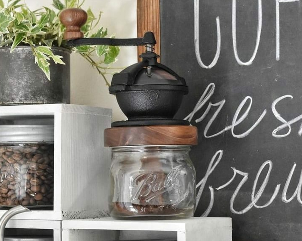 Camano Coffee Mill manual coffee grinder mounted on a mason jar sitting on a kitchen shelf beside coffee beans and a chalkboard sign
